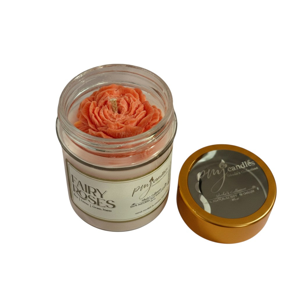 PMJ Candles Fairy Roses soy candle in a glass jar with a coral rose-shaped wax top and a gold lid.