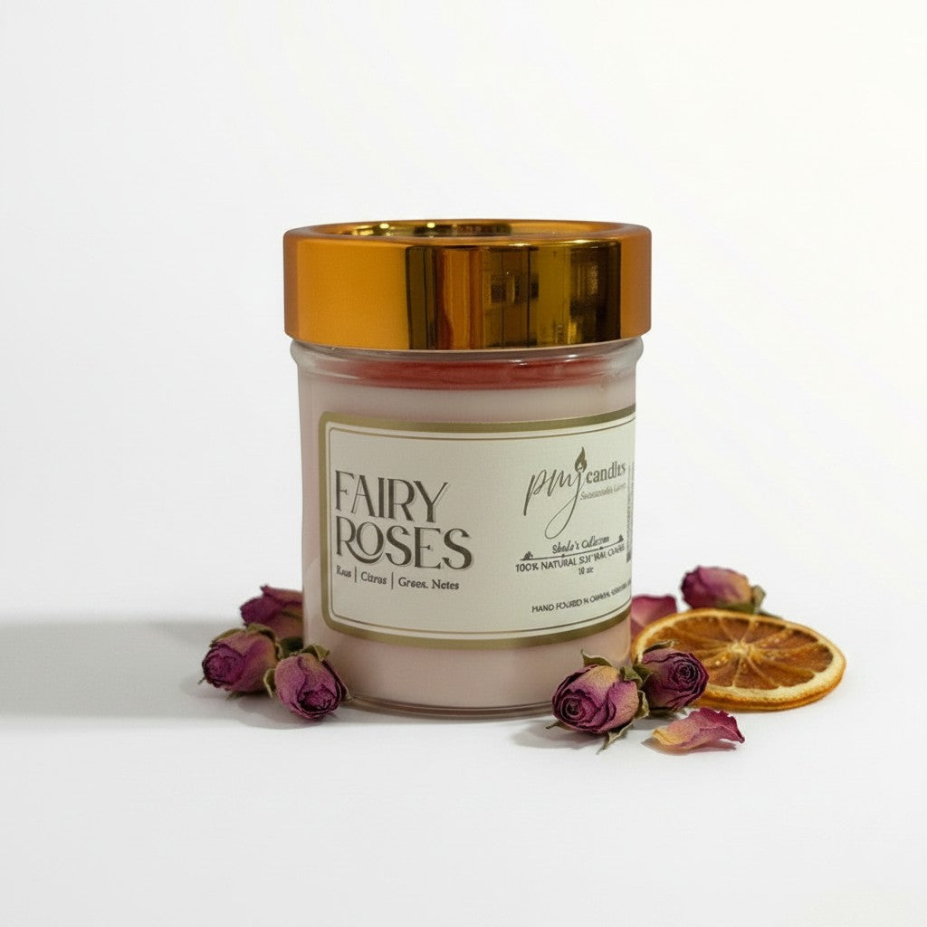 PMJ Candles Fairy Roses soy candle in a glass jar with a gold lid, surrounded by dried rosebuds and a citrus slice.