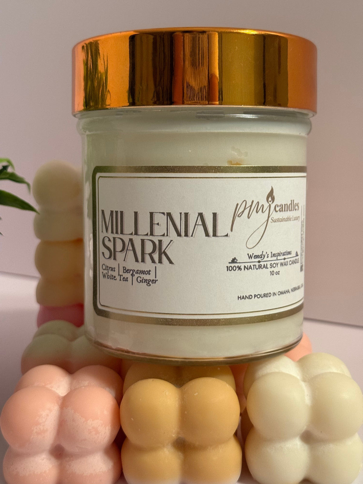 PMJ Candles Millenial Spark soy wax candle in a glass jar with a gold lid, surrounded by pastel bubble wax melts.