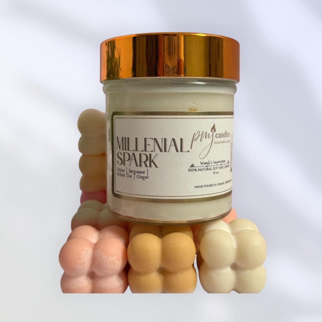 PMJ Candles Millenial Spark soy wax candle in a glass jar with a metallic gold lid, surrounded by pastel wax melts.