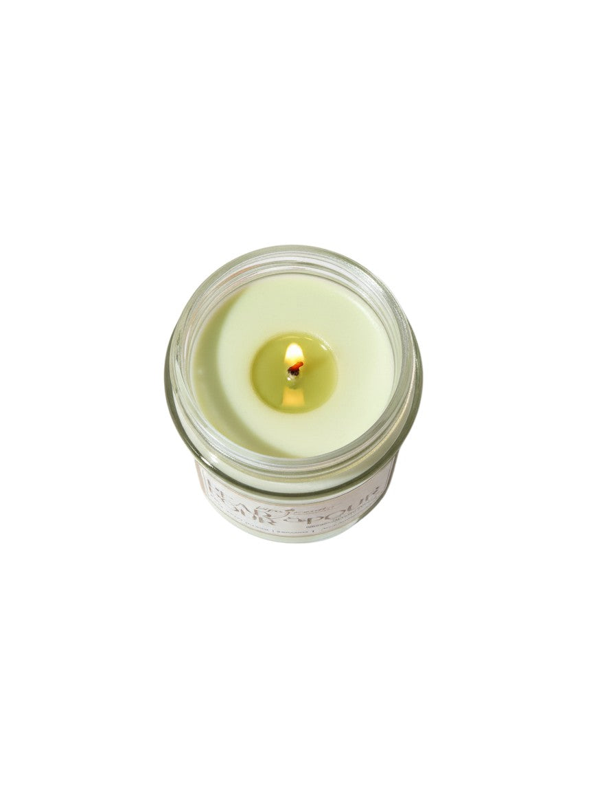 PMJ Candles Pear & Pour soy wax candle in a glass jar with a lit cotton wick, featuring a light green wax surface.