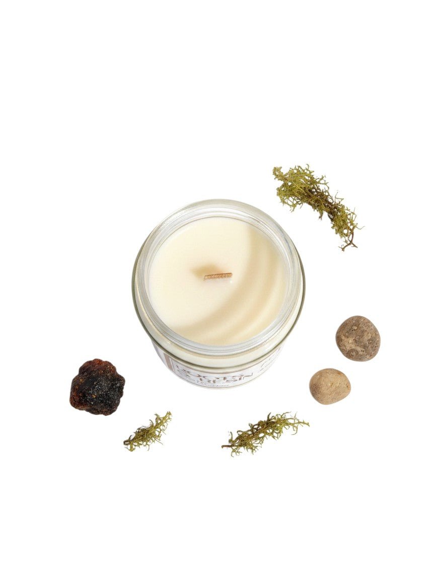 PMJ Candles Roots and Resin scented candle in a glass jar with wooden wick, surrounded by moss and stones.